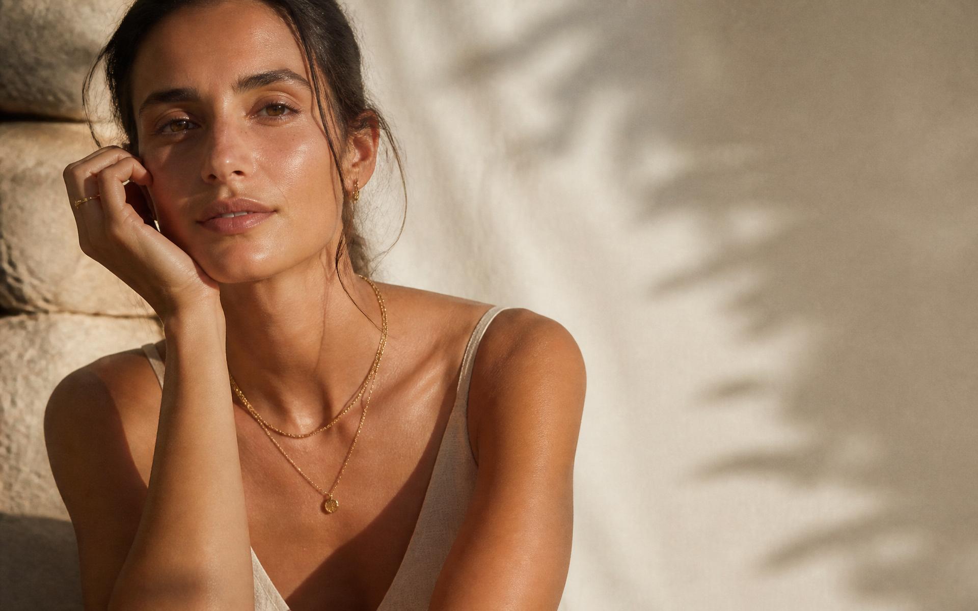 LOREVA — a woman wearing layered champagne gold necklaces in golden Mediterranean light